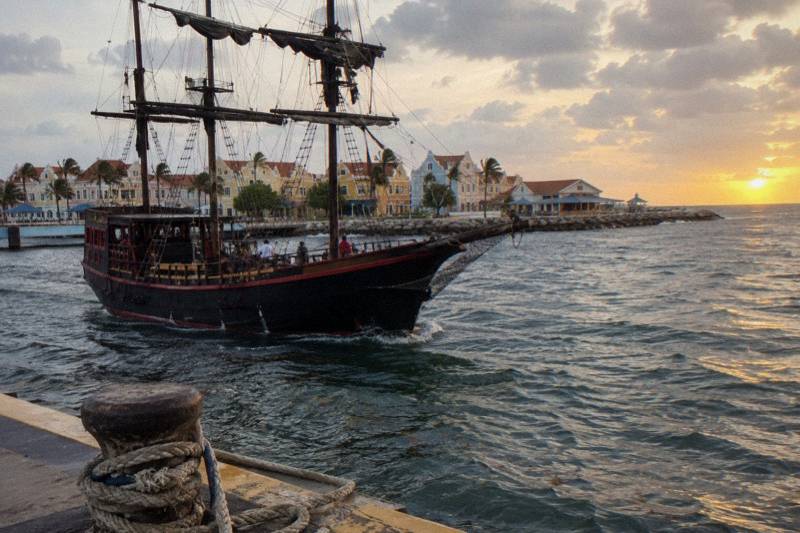 Black-hulled pirate-style sailing ship under sail off Aruba at sunset